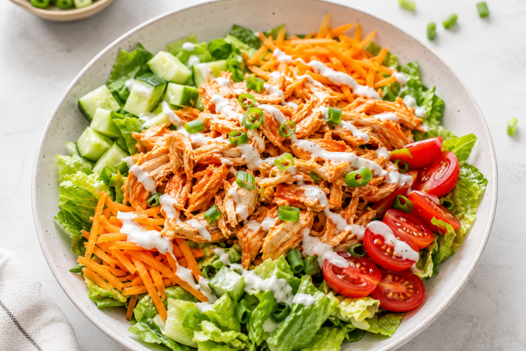 Buffalo rotisserie chicken ranch salad bowl with romaine lettuce, cucumber, cherry tomatoes, shredded carrots, green onions, and light ranch drizzle.