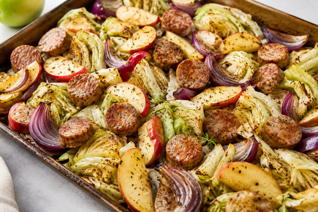 Chicken sausage, cabbage and apple sheet pan dinner under 400 calories with roasted cabbage wedges, sliced chicken sausage, red onion, apples, and herbs.